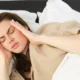 Junge Frau ist in einem dunklen Zimmer wach im Bett und blickt zur Decke – ein Symbol für Schlaflosigkeit.
