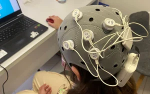 HD-tDCS-Aufbau für Schmerzprotokoll III: Helm mit Elektroden und Kabeln neben einem Computer.