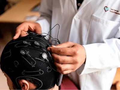 Eine medizinische Fachkraft passt einer Patientin oder einem Patienten eine Kappe mit Elektroden und Kabeln für die tDCS-Stimulation an.