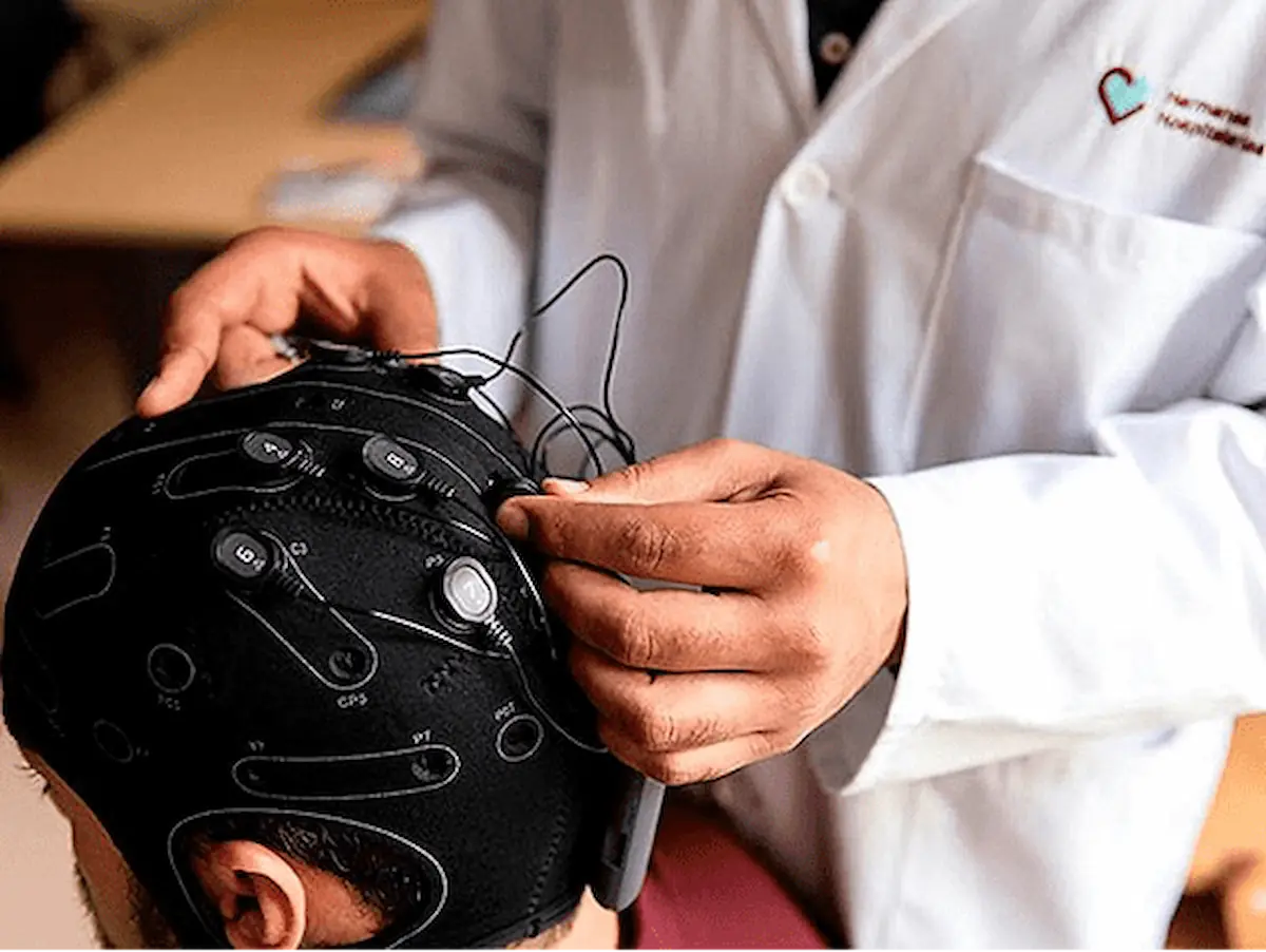 Eine medizinische Fachkraft passt einer Patientin oder einem Patienten eine Kappe mit Elektroden und Kabeln für die tDCS-Stimulation an.