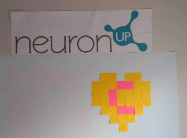 Affiche avec le logo NeuronUP sur papier, montrant un cœur formé de notes adhésives jaunes avec une touche de rose.
