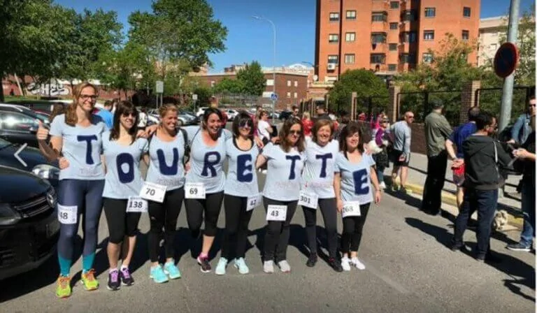 Groupe de femmes portant des t-shirts TOURETTE et des numéros sur la poitrine, en milieu urbain, montrant du soutien et de la sensibilisation.