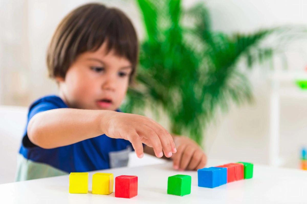 Petit garçon concentré devant une table avec des blocs de couleurs, évaluant des compétences visuo-spatiales.
