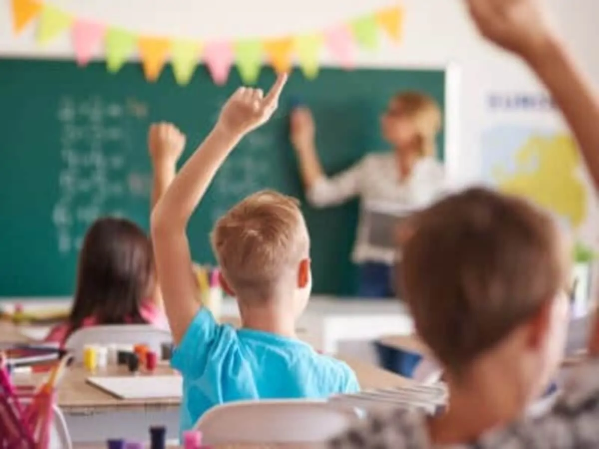 Groupe d'enfants en classe, attentifs et impliqués, tandis qu'une enseignante écrit au tableau