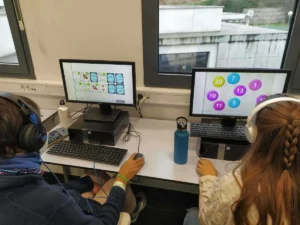 Deux enfants dans une salle de classe équipés de casques participent à la téléréhabilitation avec NeuronUP devant des ordinateurs.