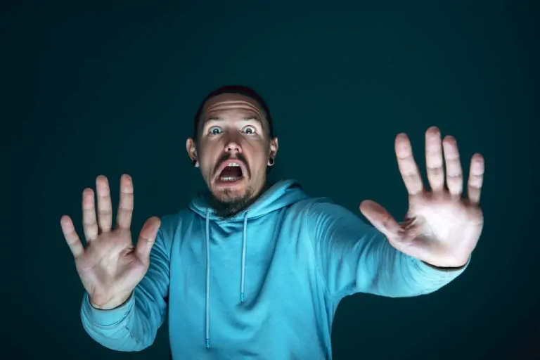 Gros plan sur un jeune homme caucasien, expression effrayée, sweat bleu à capuche, fond sombre, lié au cerveau et aux phobies.