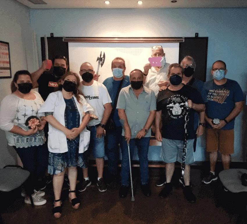 Groupe de réhabilitation neuropsychologique de la lésion cérébrale acquise Groupe de patients et de professionnels dans une salle clinique, portant des masques, observant du contenu pour la rééducation cognitive.