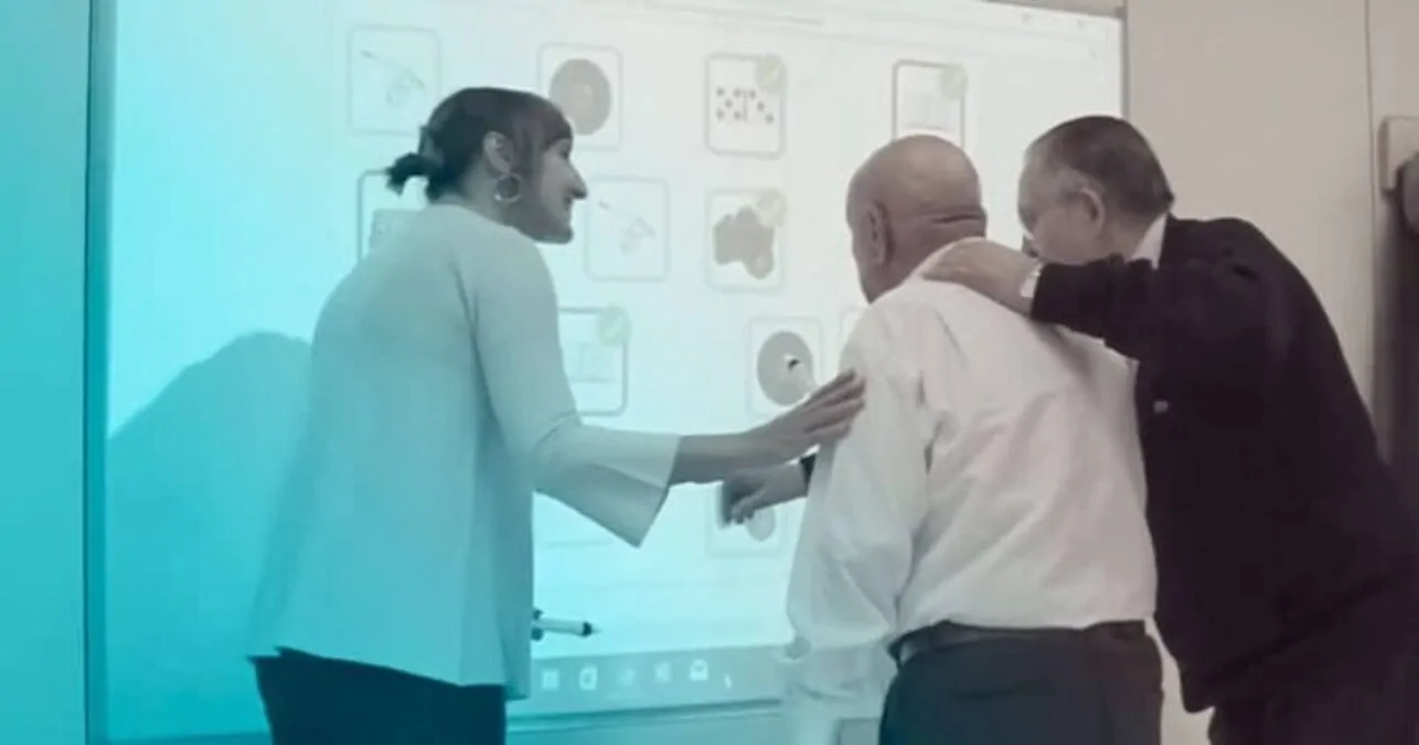 Groupe de trois personnes âgées interagissant lors d'une séance de stimulation cognitive avec des cartes d’exercices devant un écran.