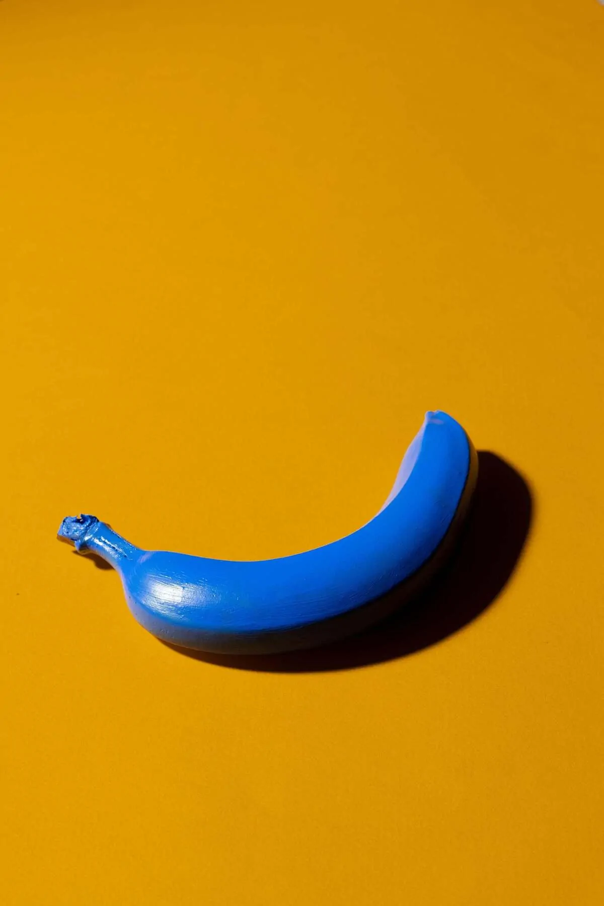 Banane bleue peinte sur un fond jaune, créant un contraste visuel saisissant et une touche surréaliste sur la diapositive.