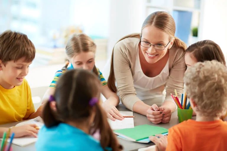 Groupe d'enfants autour d'une table, enseignant expliquant des stratégies pour le TDAH, entourés d'affiches et de supports visuels