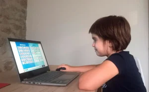 Une fille assise devant un ordinateur portable, interagissant avec une activité éducative sur les lettres à l'écran, dans un environnement intérieur.