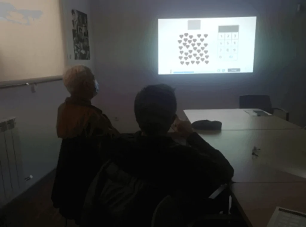 Deux personnes assises regardent un projecteur qui affiche un graphique de formes et de chiffres, avec des cœurs, dans une salle de réunion.
