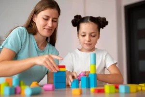 Femme et fille jouant avec des blocs de couleurs sur une table; image éducative illustrant l'interaction et le développement de l'enfant.