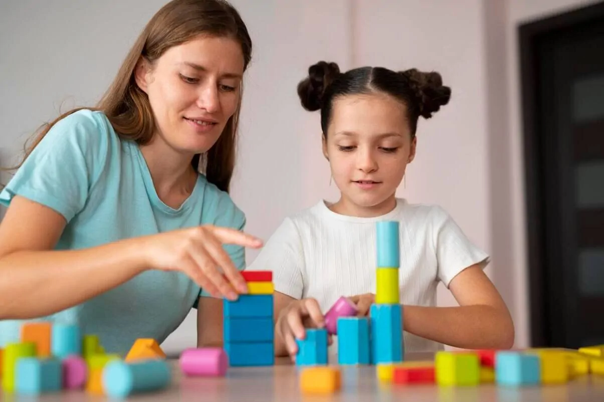 Femme et fille jouant avec des blocs de couleurs sur une table; image éducative illustrant l'interaction et le développement de l'enfant.