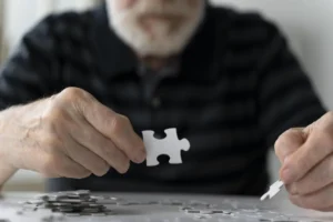 Personne âgée résolvant un puzzle ; pièces dispersées, éclairage doux et environnement calme.