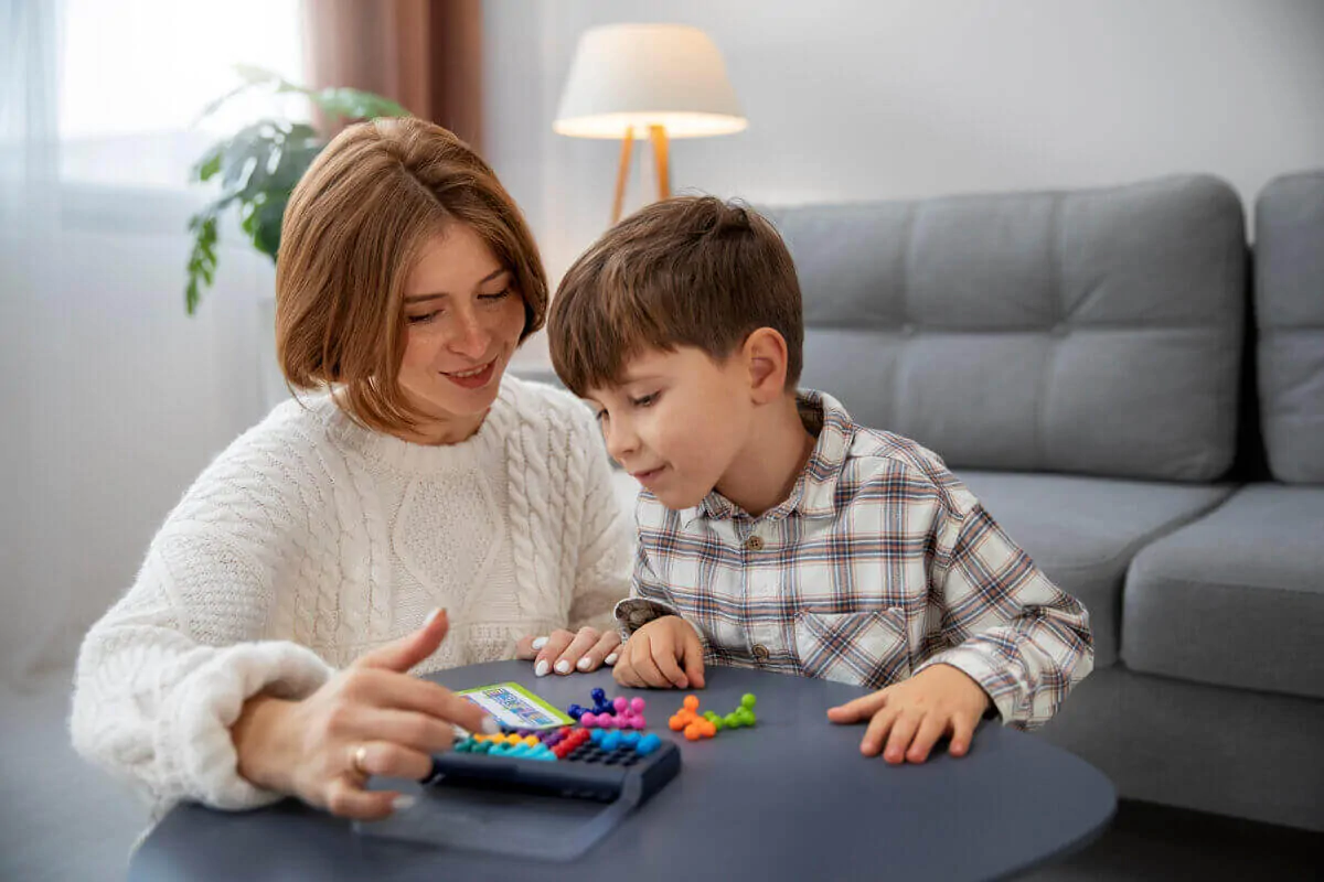 Femme et enfant interagissent lors d'une activité éducative autour d'une table, dans un cadre domestique avec des pièces colorées.