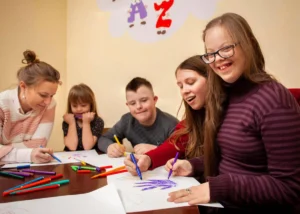Groupe divers d'élèves et une enseignante participent à une activité de dessin avec des feutres de couleur dans une classe inclusive.