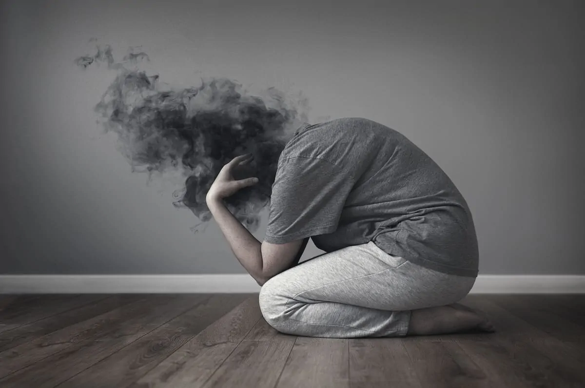 Illustration éducative d'une personne anxieuse à genoux, la tête floue dans un nuage sombre ; fond gris et surface en bois.