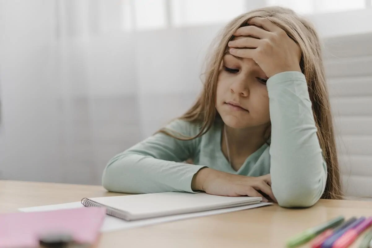 Fille en classe, avec un cahier et du matériel, expression de concentration et de frustration; l'accent est mis sur le TDAH et le fonctionnement exécutif.
