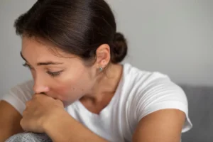 Femme assise, expression inquiète, doigt dans la bouche; image pour l'évaluation neuropsychologique de la schizophrénie.