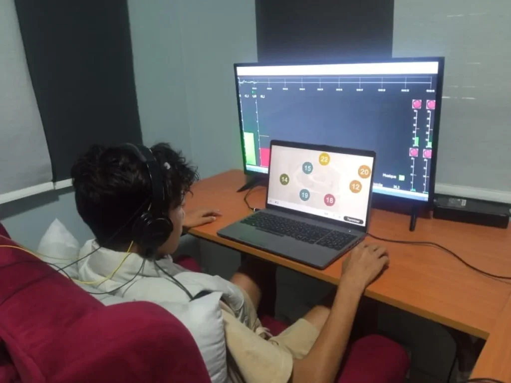 Personne concentrée devant un ordinateur et un écran avec des données, portant un casque, lors d'une rééducation cognitive BIQAF.