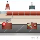 Scène dans un aéroport avec tapis roulant à bagages, plusieurs valises (vertes et rouges) et un chariot ; l'interface de NeuronUP indique une tâche de collecte de bagages sur une tablette.