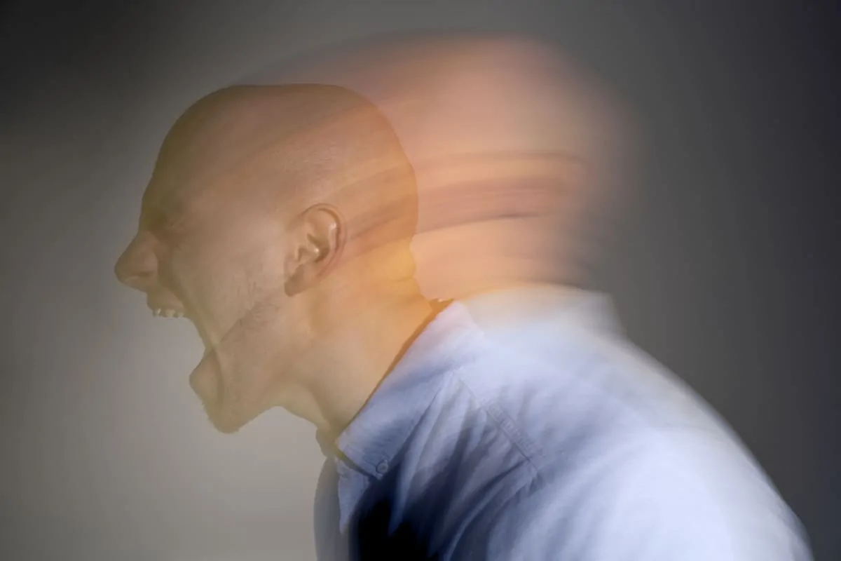 Uomo con la testa sfocata che urla, schizofrenia in primo piano; effetto movimento su sfondo neutro.