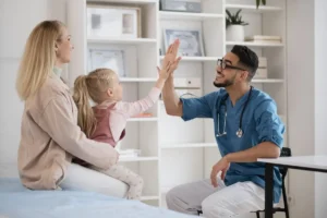 Il medico in consulto pediatrico sorride e dà un high five a una bambina, mentre la sua madre osserva in un contesto clinico.