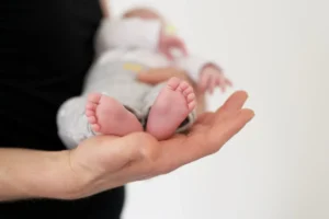 Mano di adulto che sostiene un neonato, in primo piano sui piedi rosati e sulle dita ben definite, illuminati da una luce soffusa.