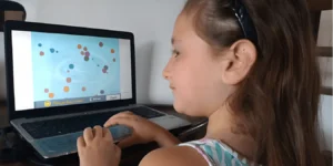 Bambina seduta di fronte a un portatile, con una fascia sulla testa, che interagisce con NeuronUP.