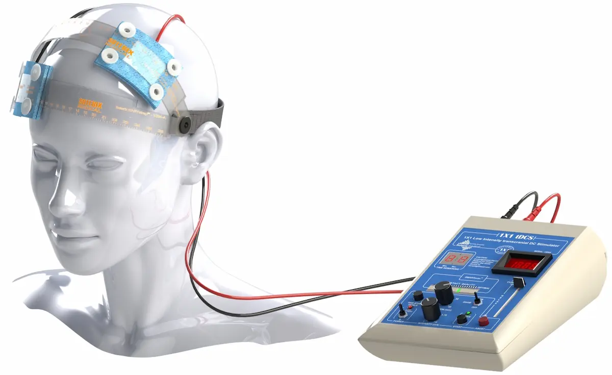 Dispositivo di stimolazione cerebrale su modello di testa: elettrodi frontali collegati a un apparecchio con pulsanti, manopole e display.