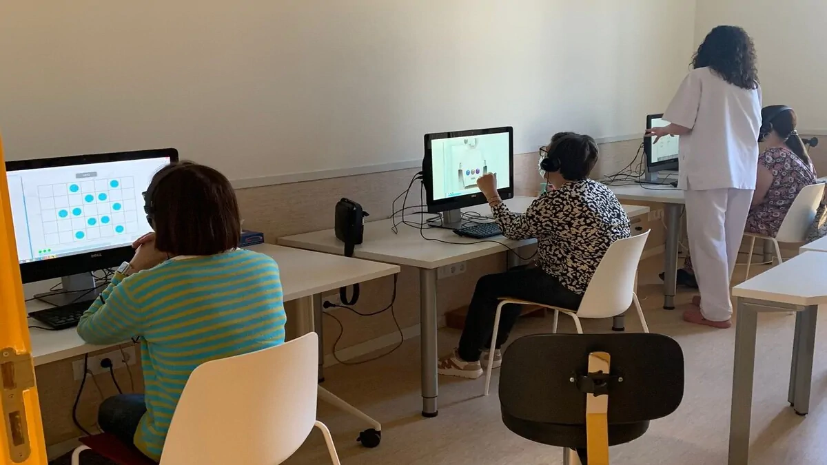 Gruppo di donne sedute davanti a computer con cuffie, mentre un’istruttrice in piedi osserva e aiuta durante una sessione di apprendimento NeuronUP.