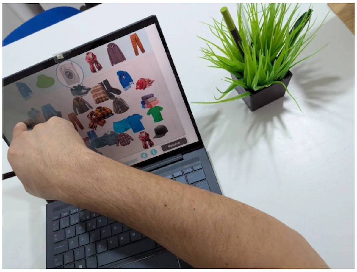 Professionista di psicologia e neuropsicologia di fronte a un laptop su una scrivania bianca, che segnala uno schermo con capi di abbigliamento e una pianta.