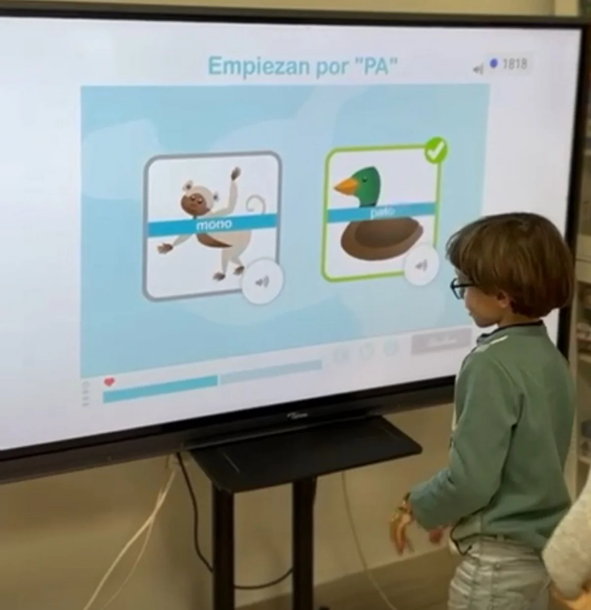 Bambino interagisce davanti a uno schermo durante una sessione di NeuronUP; si vede una scimmia e un'anatra, con un esercizio di parole che iniziano con PA.