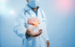 Medico in camice bianco e mascherina sostiene una rappresentazione tridimensionale di un cervello illuminato; sfondo clinico o tecnologico.