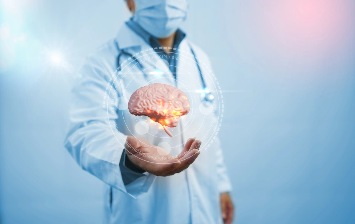 Medico in camice bianco e mascherina sostiene una rappresentazione tridimensionale di un cervello illuminato; sfondo clinico o tecnologico.