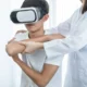 Молодой человек в VR-шлеме, сосредоточенно выполняющий упражнение; специалист поддерживает его руки во время реабилитации.