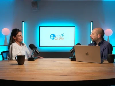 Д-р Дженни Лубрини беседует в NeuronUP Talks в студии звукозаписи; на заднем плане микрофоны и экран с надписью Teatro Talks.